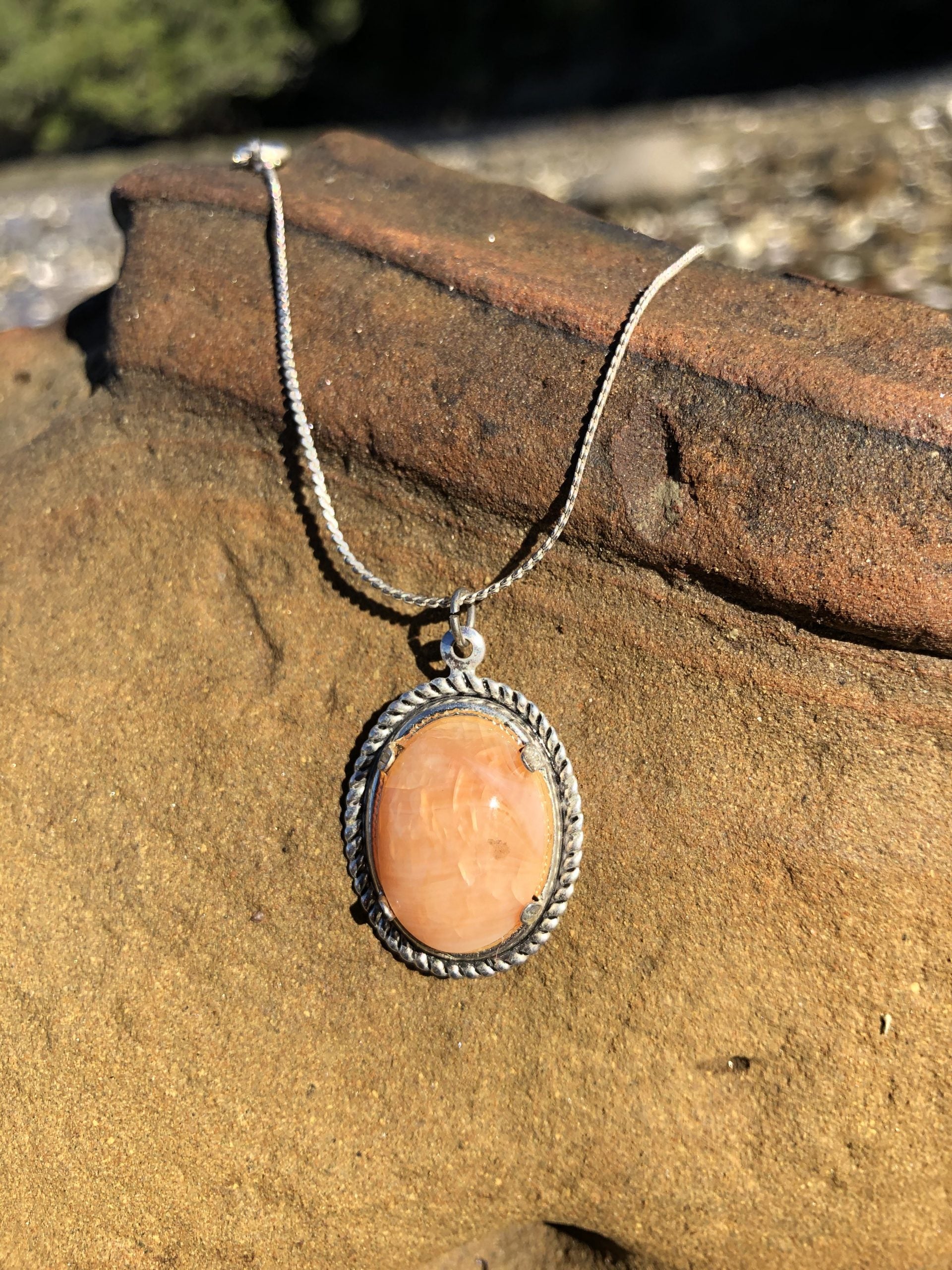 Necklace of Tangerine Agate from Agate Creek, Australia, natural tangerine orange color, hand polished to an 18x13mm cabochon and set in silver plated setting with 19 inch chain on rocks