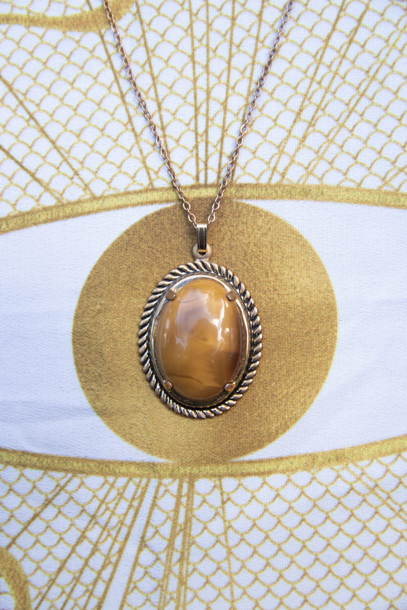 Necklace with a natural New Zealand Carnelian, with sparkling translucent orange glowing through swirling browns, hand polished to a 25x18mm oval cabochon and set in a gold plated setting with 19 inch chain, front