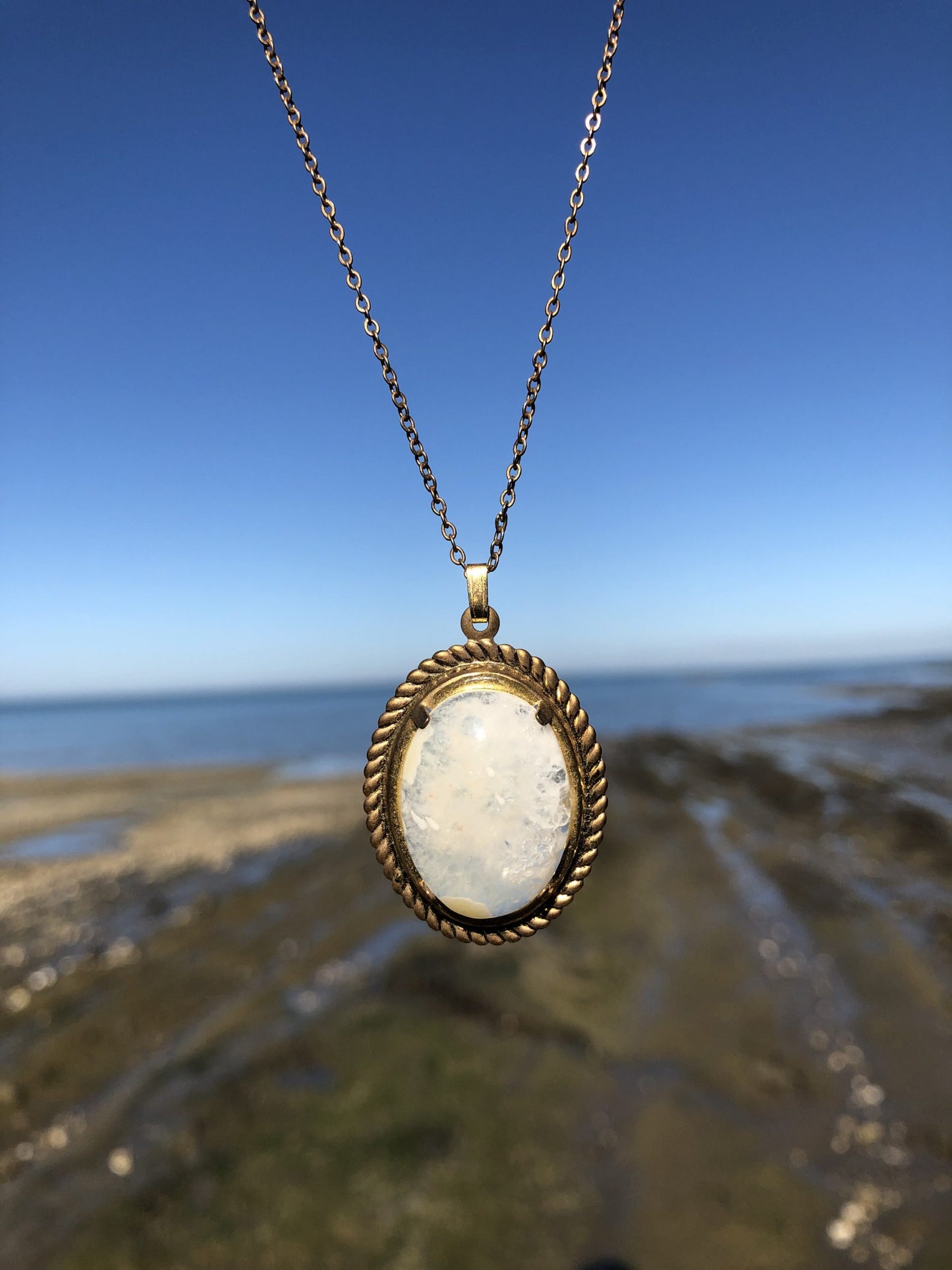 Necklace of sparkling New Zealand quartz from the heart of a solid geode, hand polished to a 25x18mm oval cabochon and set in a gold plated setting with 19 inch chain, on beach