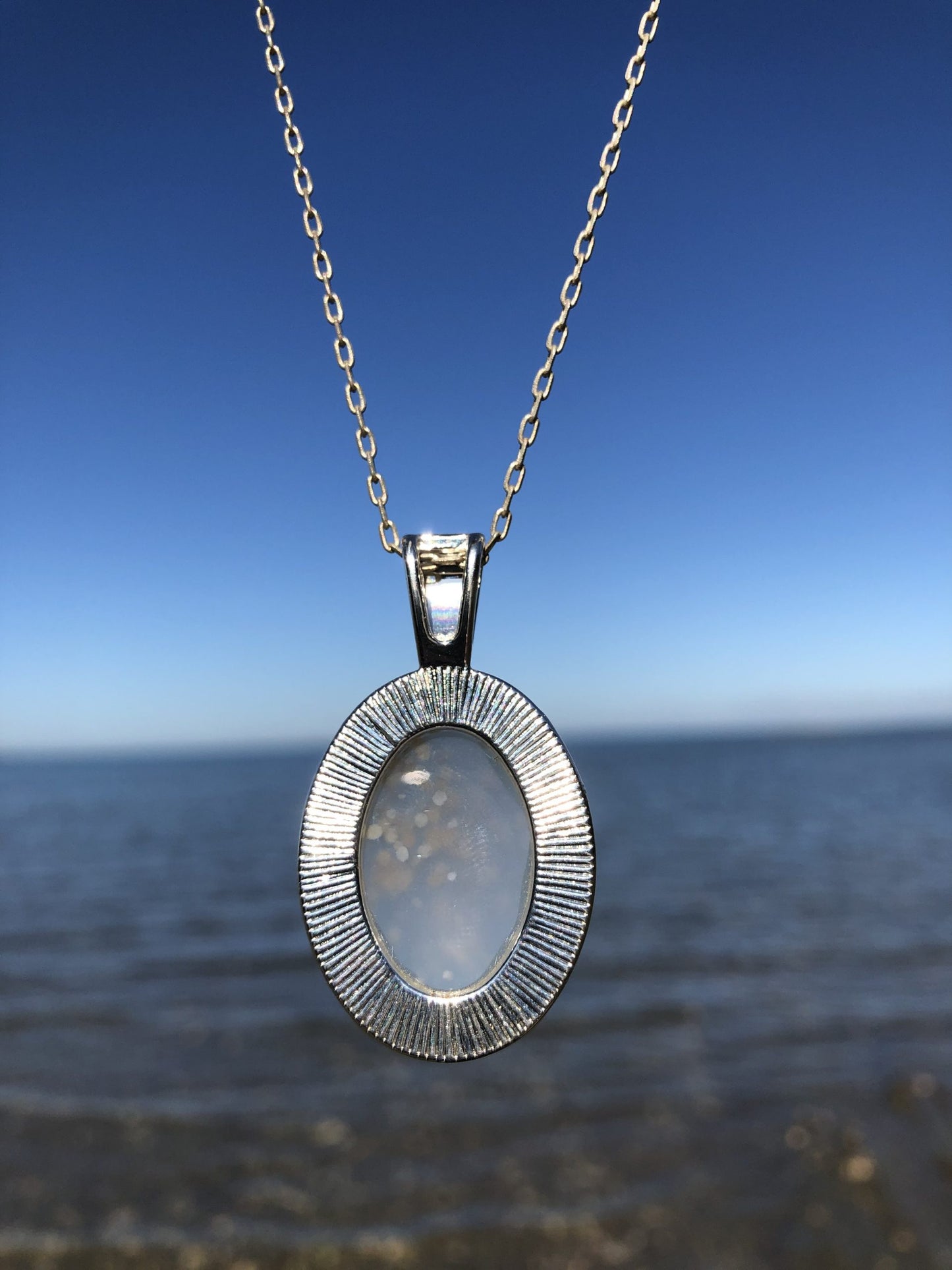 Necklace with natural petrified wood from Matauri Bay, New Zealand, showing delicate pale blue with dots (bubbles) of tan and brown, hand polished to a 25x18mm cabochon and set in a silver plated setting with 19 inch chain, back