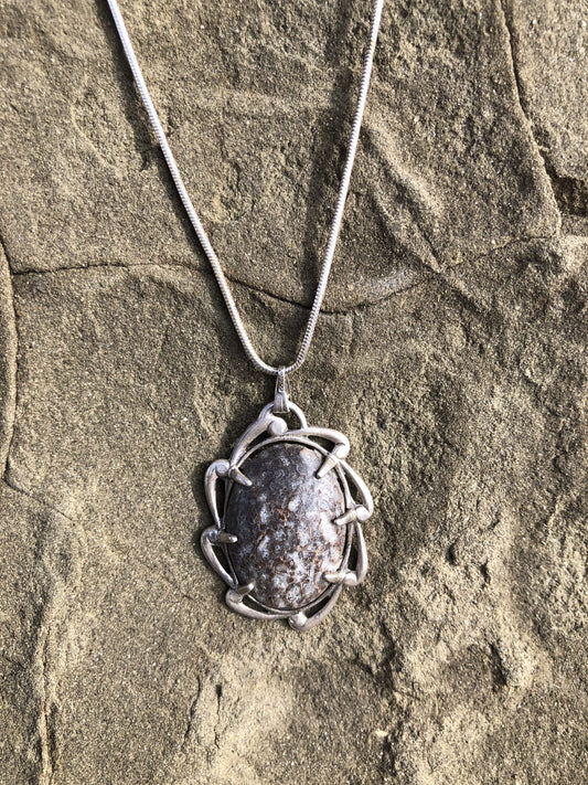 Necklace with real, natural, fossilized dinosaur bone with gray, brown and white markings, hand polished to a 25x18mm cabochon and set in a sterling silver setting with a 24 inch sterling silver snake chain.