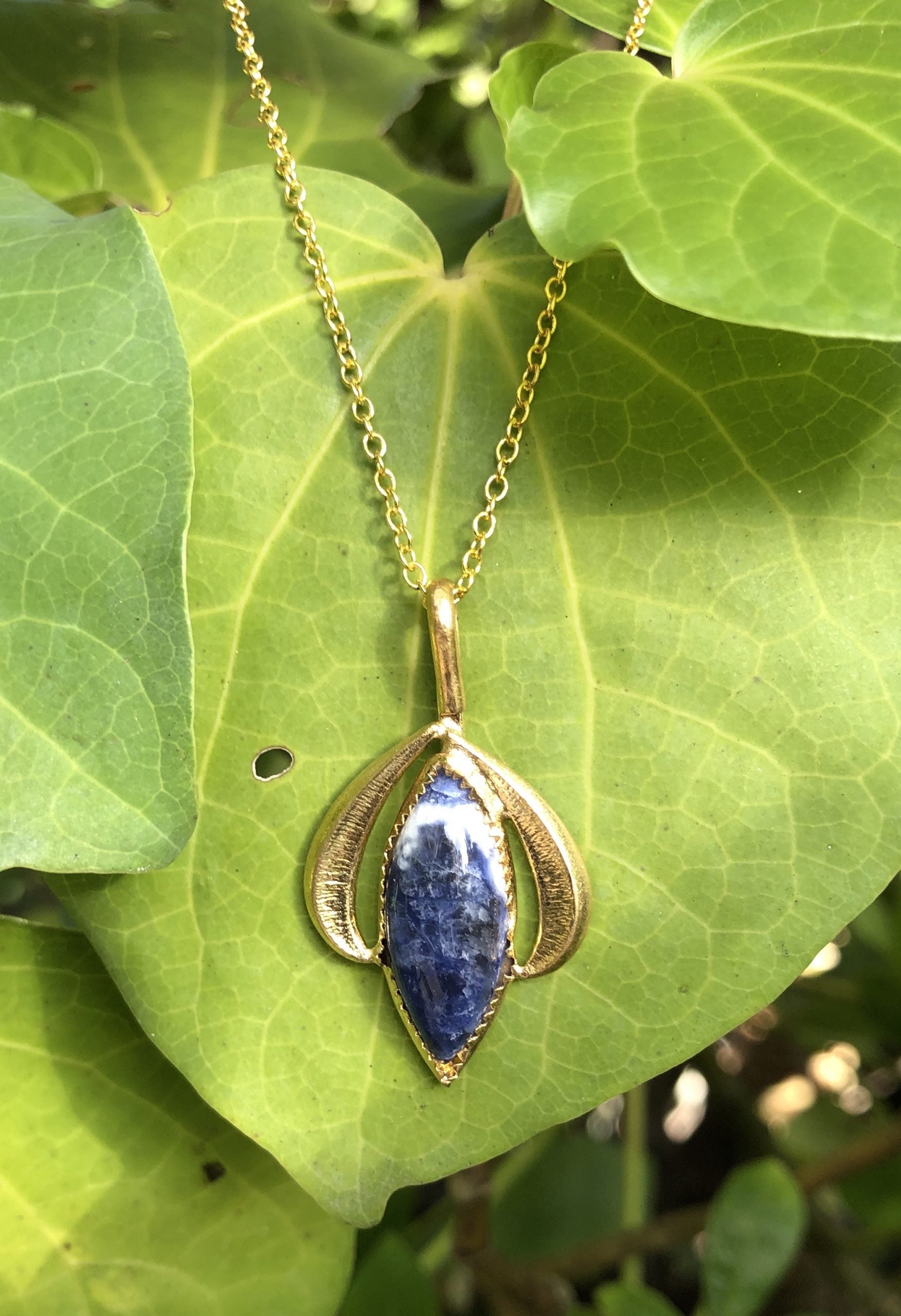 Necklace with natural blue sodalite with delicate white lace patterning, hand polished to a 24x8mm marquise cabochon and set in a gold-plated setting with 19 inch chain.